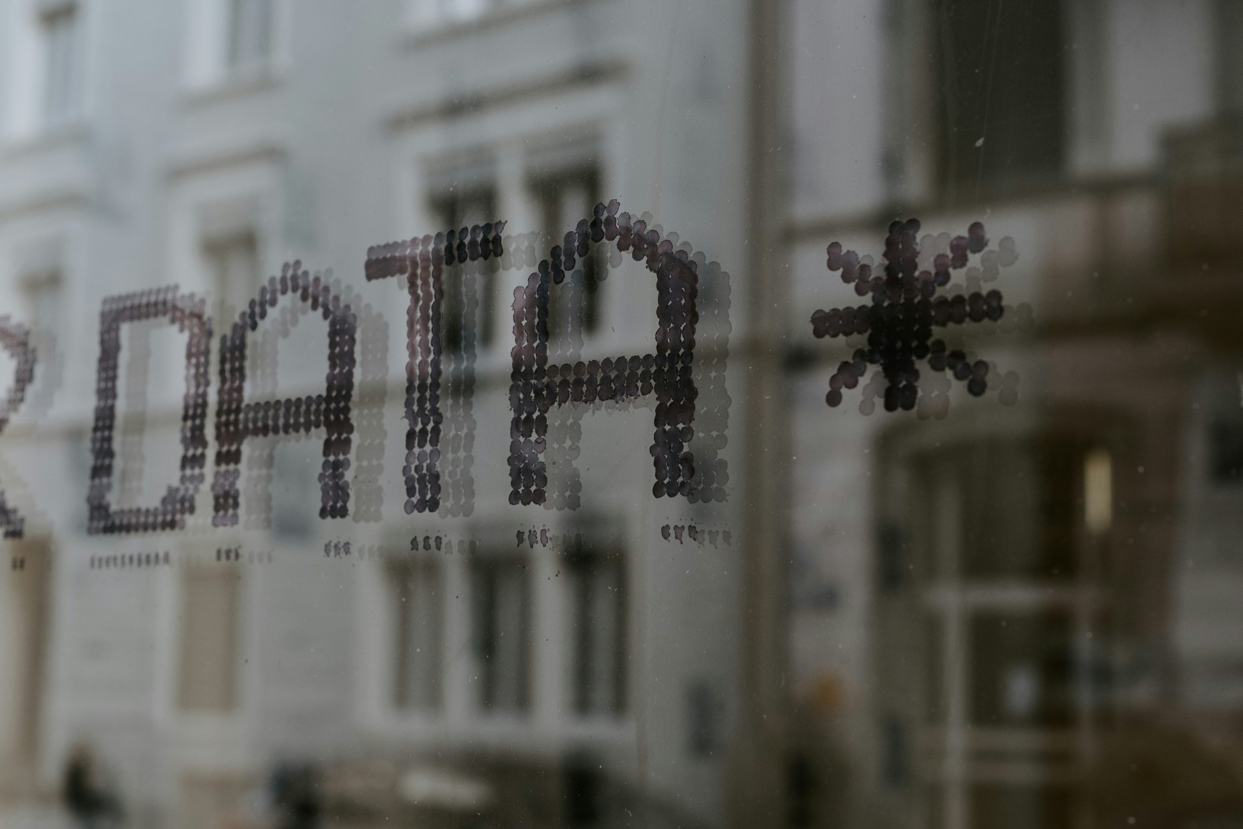 The term 'DATA' spelled out with dot stickers on a glass window, against a blurred cityscape background, illustrating the concept of data collection through web scraping.